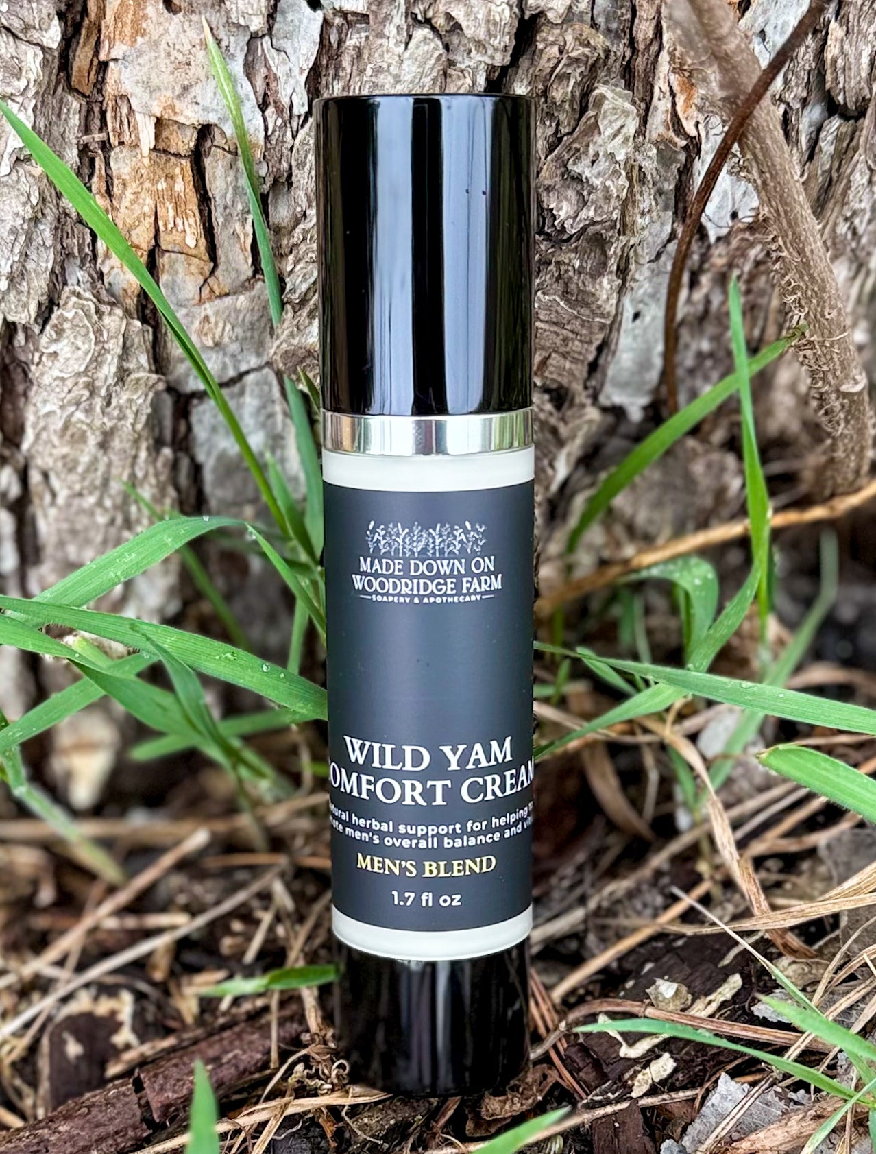 A frosted air pump bottle of Men's Blend Wild Yam Comfort Cream, set against a natural background with green leaves and wood - Naturally Linda