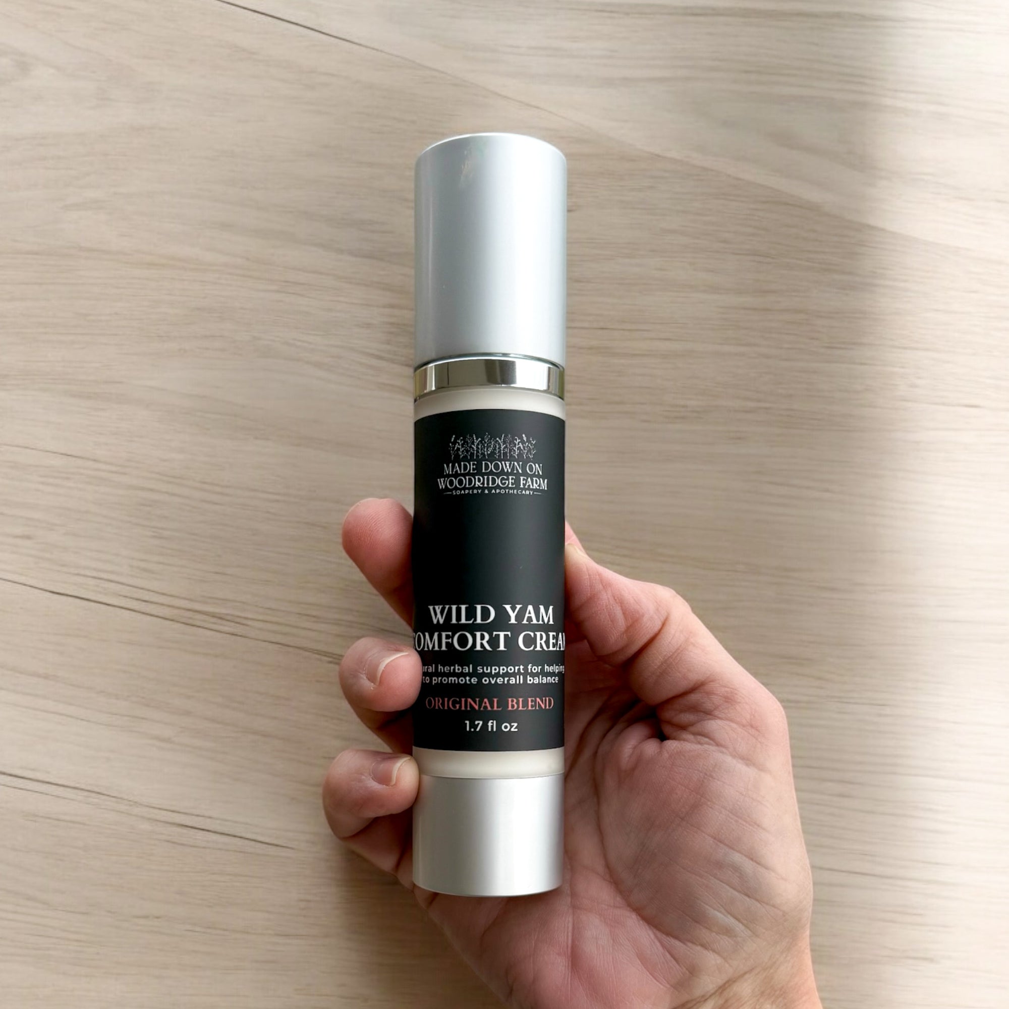 A frosted air pump bottle of Wild Yam Comfort Cream held in a hand, with a label that includes the product name and a brief description.